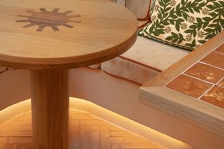 The detail of a dining room's sitting area show bespoke wooden tables covered in tiles as well as flowery cushions and decorated banquettes.