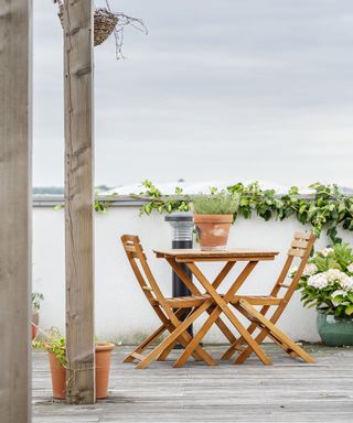 Decked roof garden ideas with a white wall and wooden bistro table and chairs.