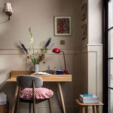 Wooden desk with flowers in vase, red desk lamp and wooden chair with red and white ruffled seat cushion