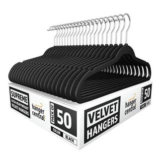 A stack of black velvet slimline hangers with silver hooks, on top of a black and white cardboard box