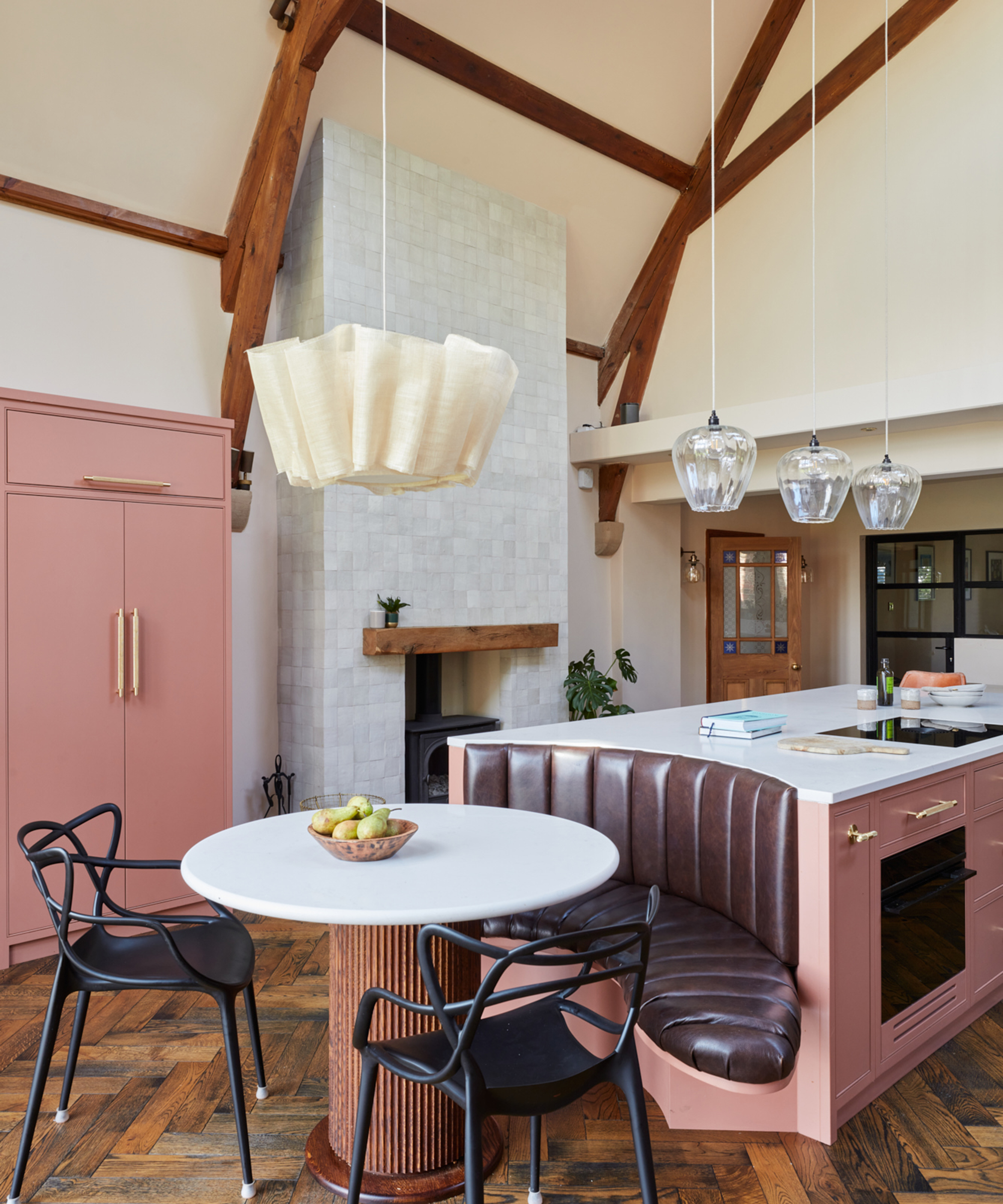 pink kitchen with herringbone wooden flooring and banquette seating with oversized pendant dining table light