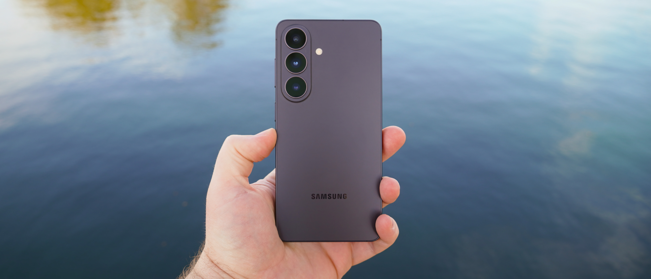 The Samsung Galaxy S26 in Black in the hand in front of a lake.