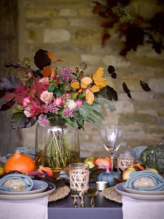Halloween fall table with blue napkins, lilac tableware, gourds and pumpkins, vase of flowers
