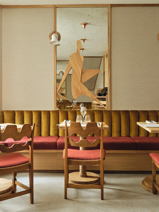 A vintage-inspired restaurant features wooden finishes informed by cubism, mid-century modern soft seating in shades of brown and red, and wooden tables as well as chairs.