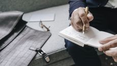 A man wearing a suit writing in a journal using a fountain pen