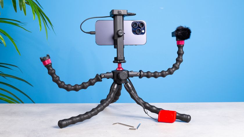 The Neewer T91 iPhone tripod with a phone attached and accessories mounted, on a stone surface with a blue background