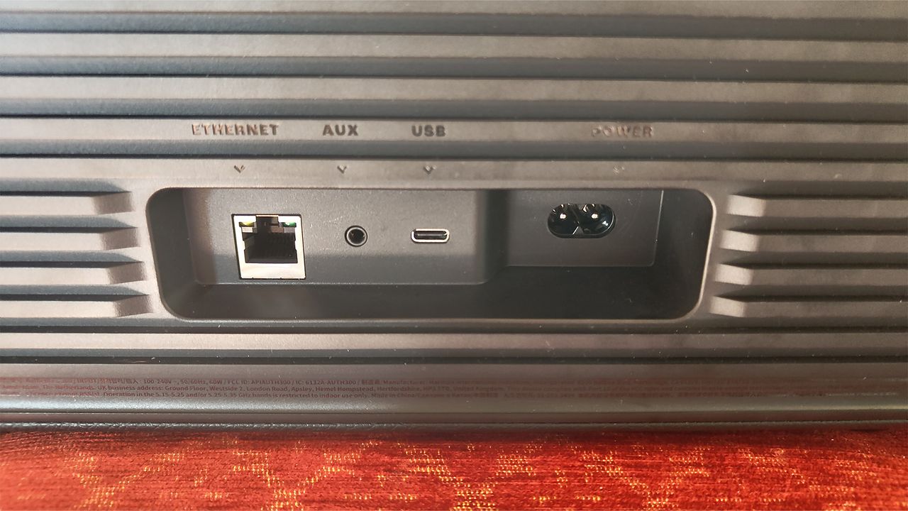 A close-up of the inputs on a black JBL Authentics 300 wireless speaker. There is a square ethernet port, a circular aux in, an oval-shaped USB-C port, and a figure-of-eight style power socket.