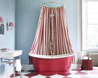 A master bathroom with blue walls, a red freestanding tub with a red and white striped shower curtain, and a red and white checkered floor