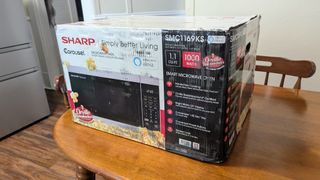 The Sharp SMC1169KS 1.1 cu. ft. 1000W Smart Stainless Steel Countertop Microwave Oven is packaged safely in a cardboard box.