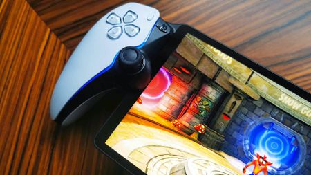 Close up of PlayStation Portal on woodgrain table with Crash Bandicoot 2 gameplay on screen.