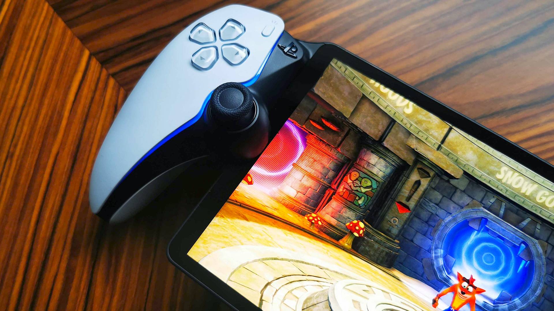 Close up of PlayStation Portal on woodgrain table with Crash Bandicoot 2 gameplay on screen.