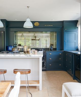 A blue painted kitchen with travertine flooring and a white kitchen island with marble countertop and pendant lighting