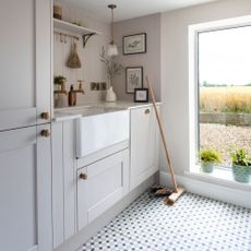 Grey utility room with cupboards and tiled flooring, with a broom and brush sitting on the floor