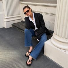 @cocoschiffer seated outfit photo in black blazer, white shirt, jeans, and black filp-flop sandalas