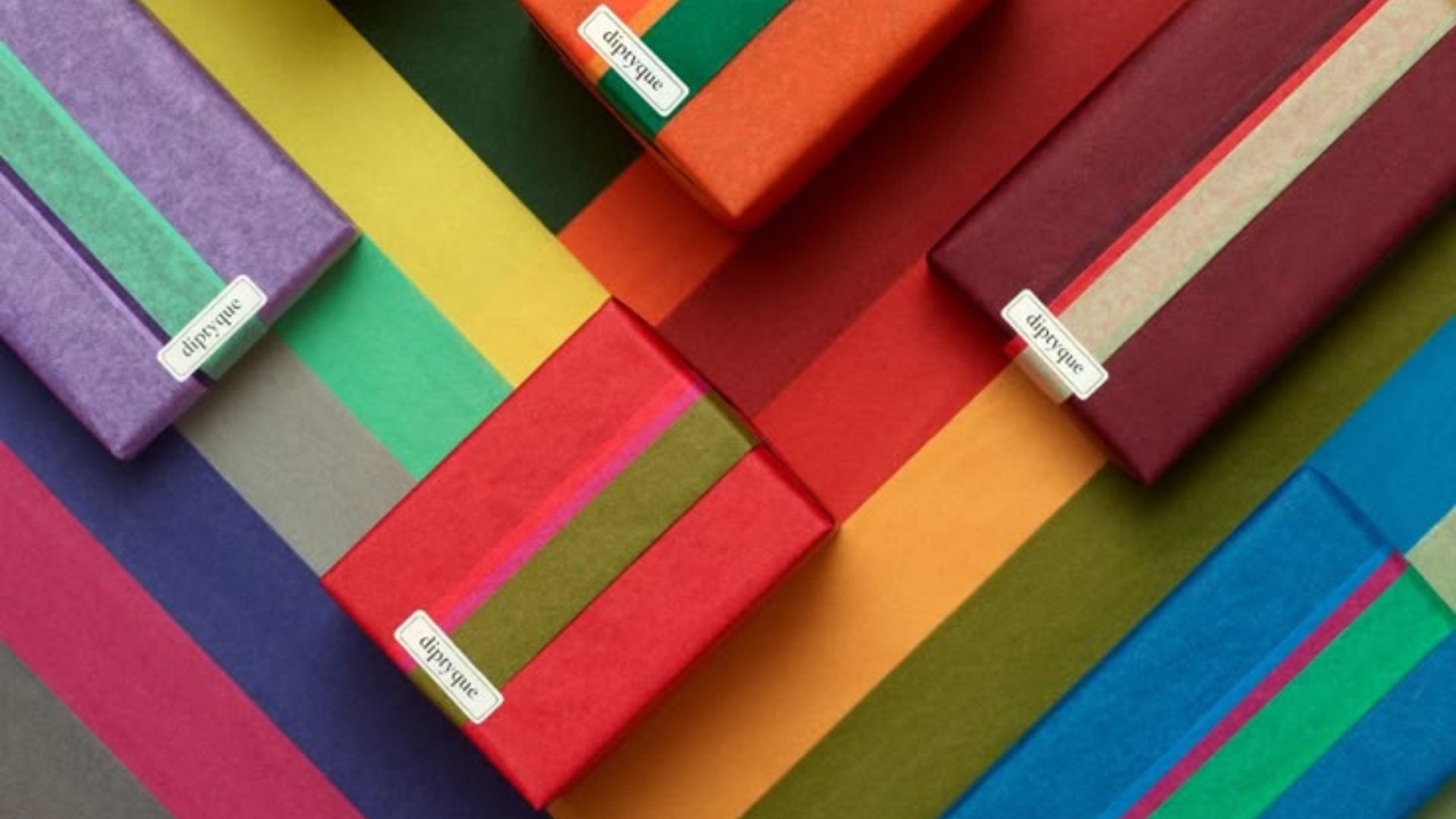 Diptyque candles wrapped on a colourful background that uses the tissue paper images