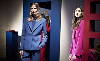 two female models, the left is wearing a blue suit and the right is wearing a pink suit