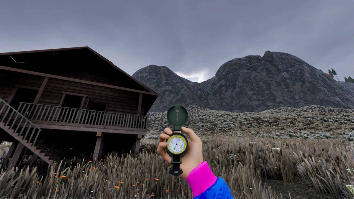 A hand holding a compass in front of a wooden cabin