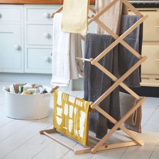 Wooden clothes airer filled with clothes next to cleaning bucket on wooden floor