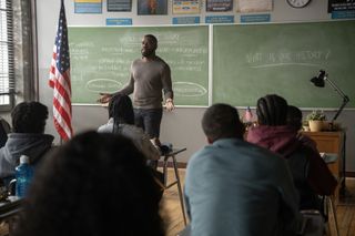 Colman Domingo as Muncie Daniels, teaching at a chalkboard in front of a class of children, with an American flag to the left and a desk to the right, in Episode 108 of 'The Madness.'