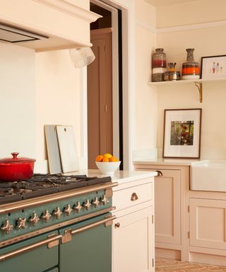 A pink kitchen with a green oven, wall art, a fruit bowl, and a red casserole dish