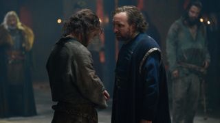 Arthur (Iain De Caestecker) in a dark tunic stands before King Uther (Eddie Marsan) in a blue robe in The Winter King.