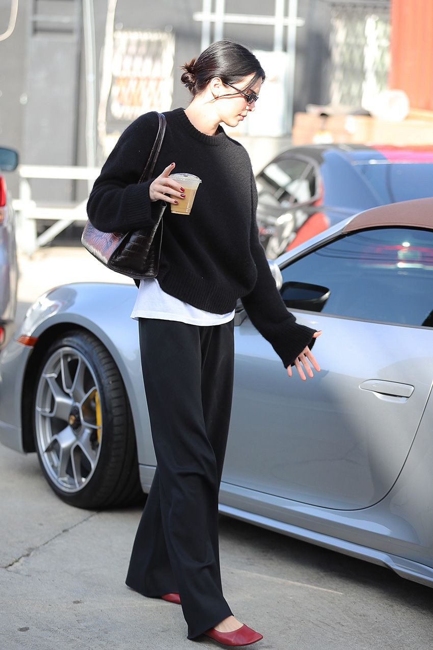 Kendall Jenner in Los Angeles wearing a black sweater, loose black pants, red The Row ballet flats, and a croc shoulder bag