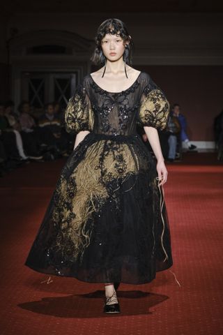 Woman on runway in black Simone dress with raffia
