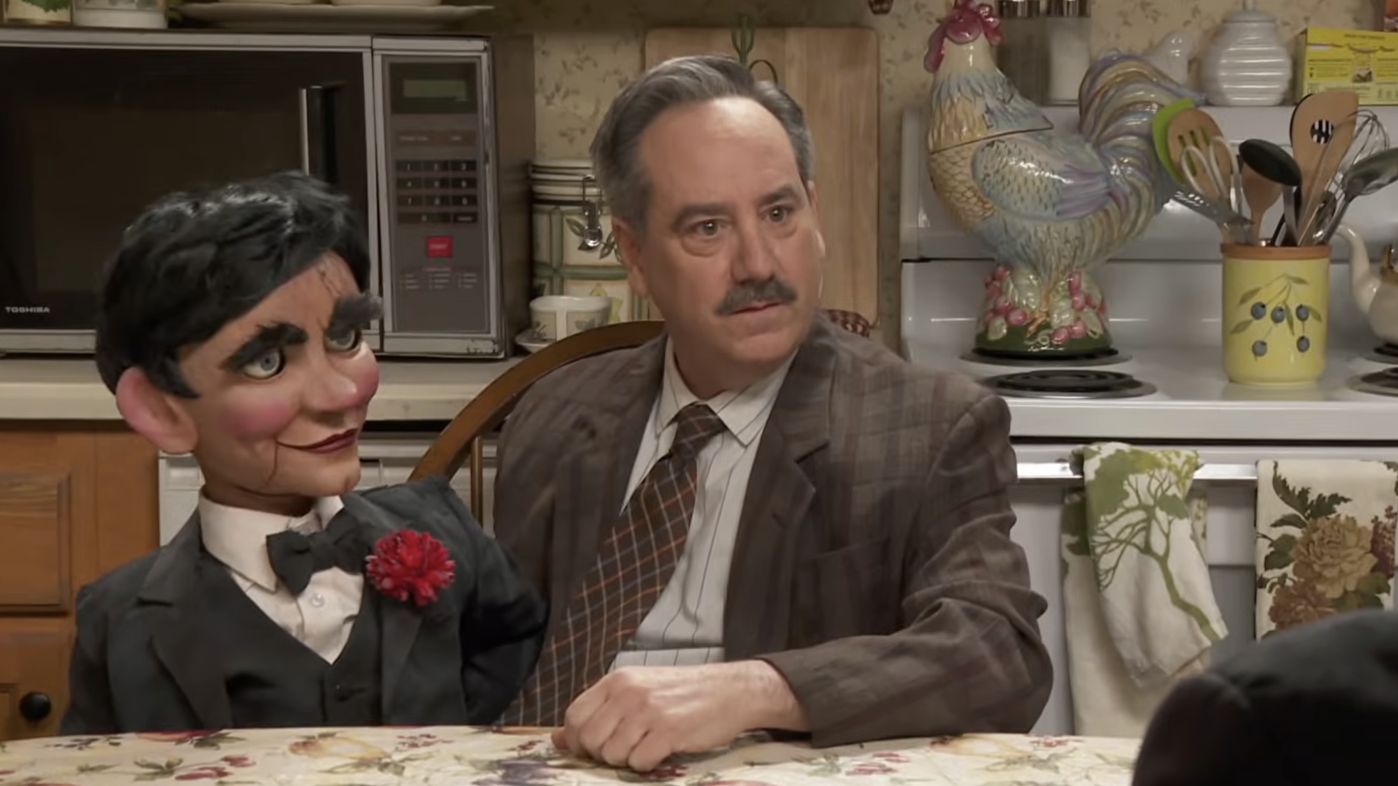 Uncle Jack Kelly sitting at kitchen table with ventriloquist dummy in It's Always Sunny in Philadelphia Season 18