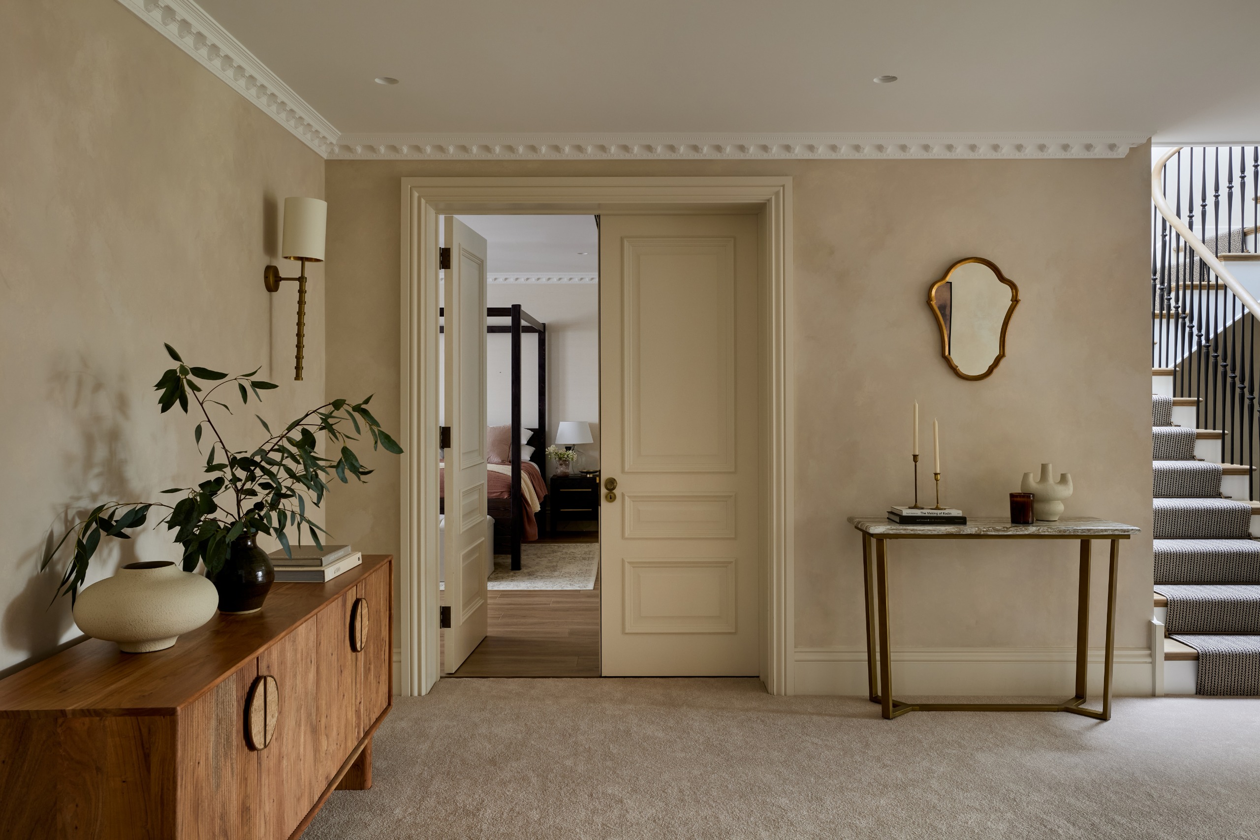 A beige-tinted hallway with wooden furniture, a neutral rug, plaster walls in earthy beige, marble details, and sleek accessories, along with stucco detailing.