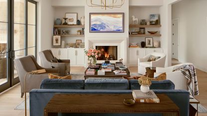 neutral living room with a fireplace, built in cupboard and shelves in the alcoves, a blue velvet couch with two boucle swivel chairs
