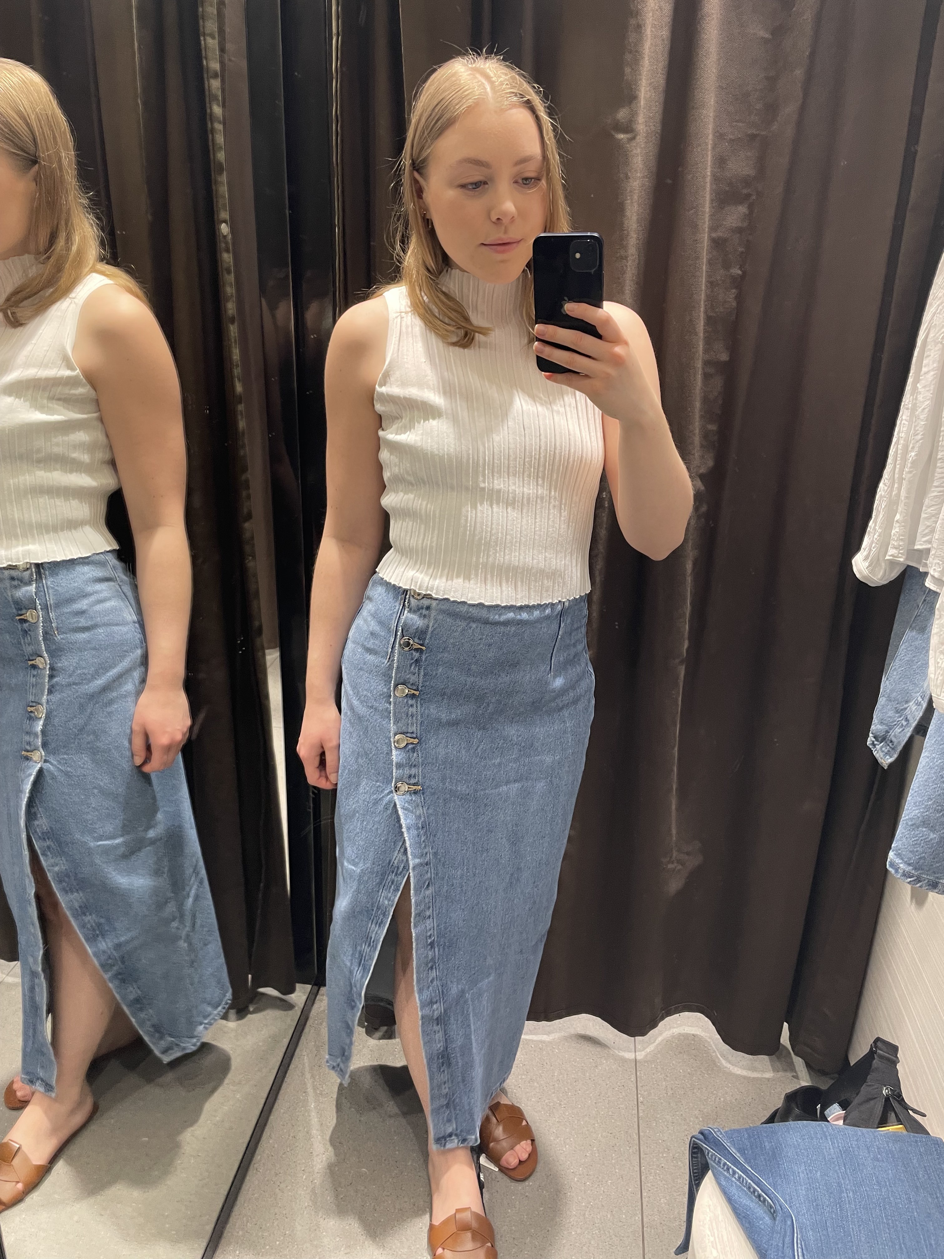 Woman in dressing room wears white top, denim skirt and brown sandals