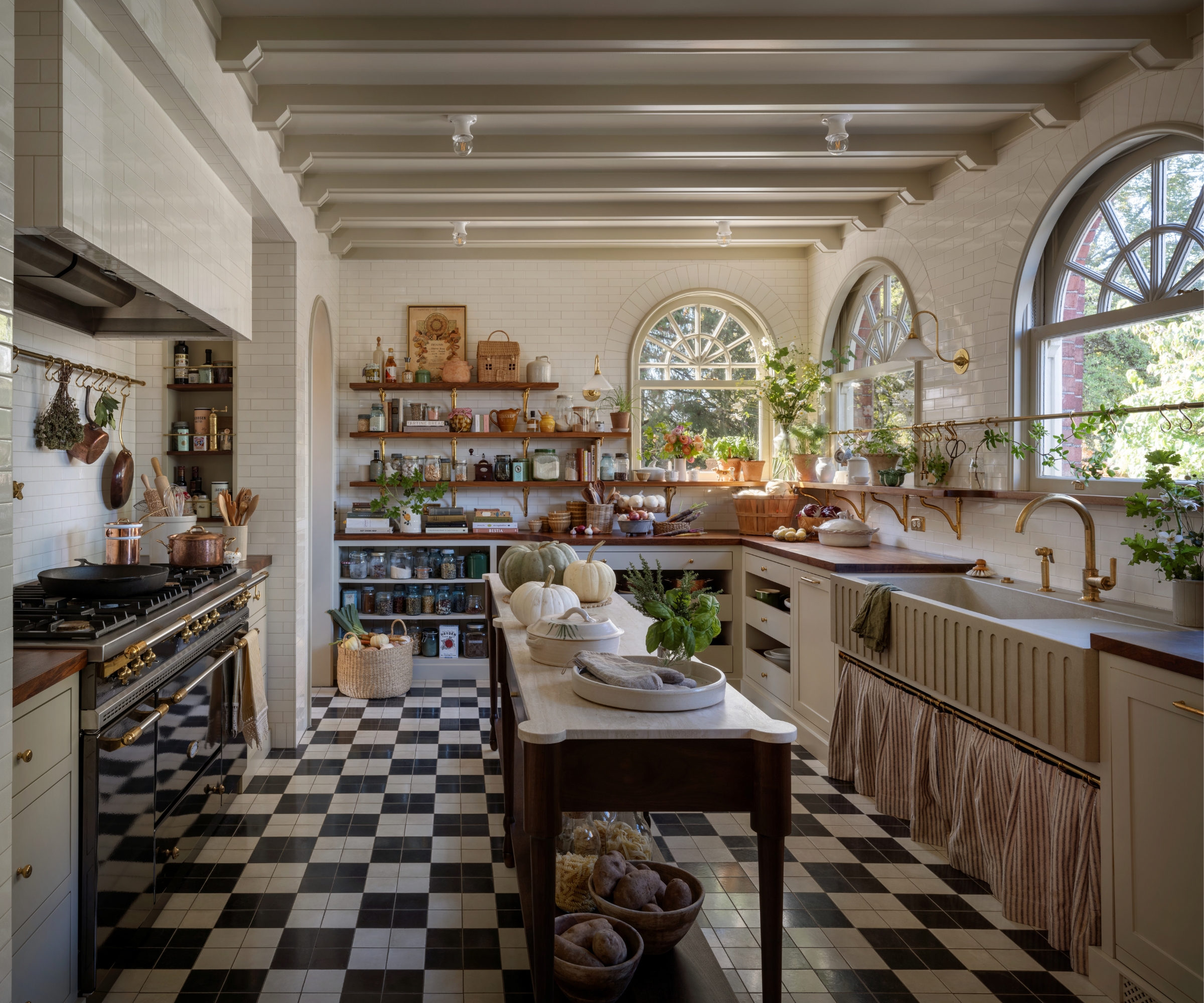 a small kitchen with warm white cabinets, white subway tiles on all the walls, a narrow freestanding wooden island, black and white checkerboard floors, and lots of open storage