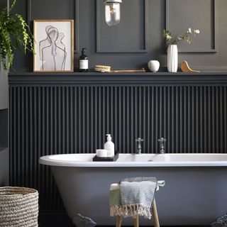 Dark bathroom with wall panelling behind grey bath