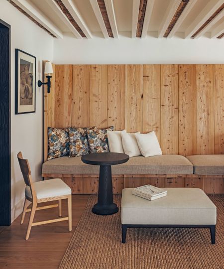 a rustic dining area in a home in France with ceiling beams, a cedar clad banquette seat and black wooden round table