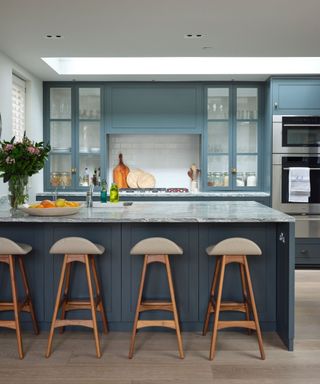 Kitchen with dark fitted cupboards, marbled work top, central kitchen island with bar stools below a skylight.