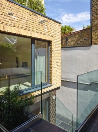 The corner of a home with a brick facade and glazed elements with glass stairs leading down to a basement extension