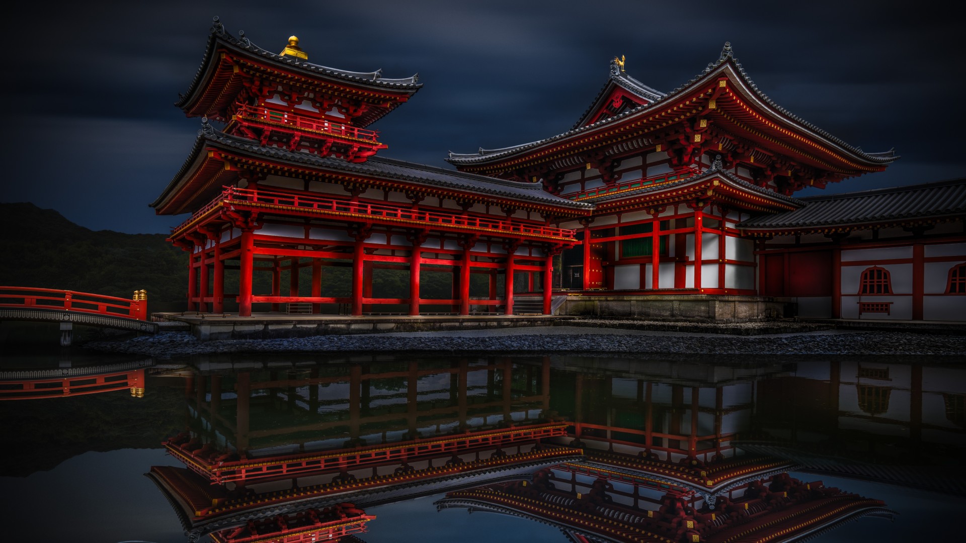 A dramatic, low-light photograph of the red and white wooden structures of the Byōdō-in Temple in Uji, Japan, reflected clearly in the dark water of a pond, with a single white koi fish near the bottom left corner.