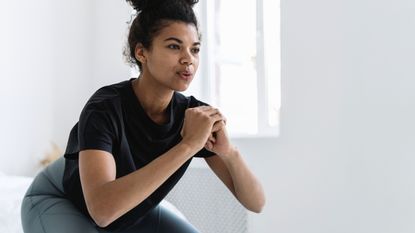 A woman performs a leg workout at home, squatting down and exhaling in a clean white room
