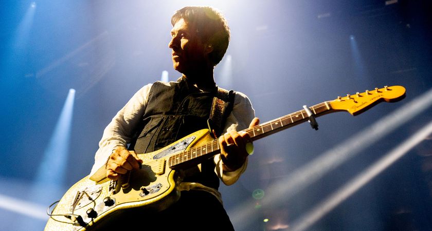 Johnny Marr plays his Fender Jaguar with a capo at the 2nd fret. His head is haloed by a white stagelight.