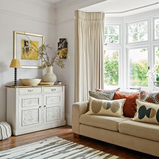 neutral living room with cream sofa and curtains, patterned cushions and decorative sideboard