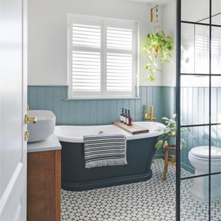 White bathroom with blue cladding on the walls, a blue bath tub and patterned floor tiles