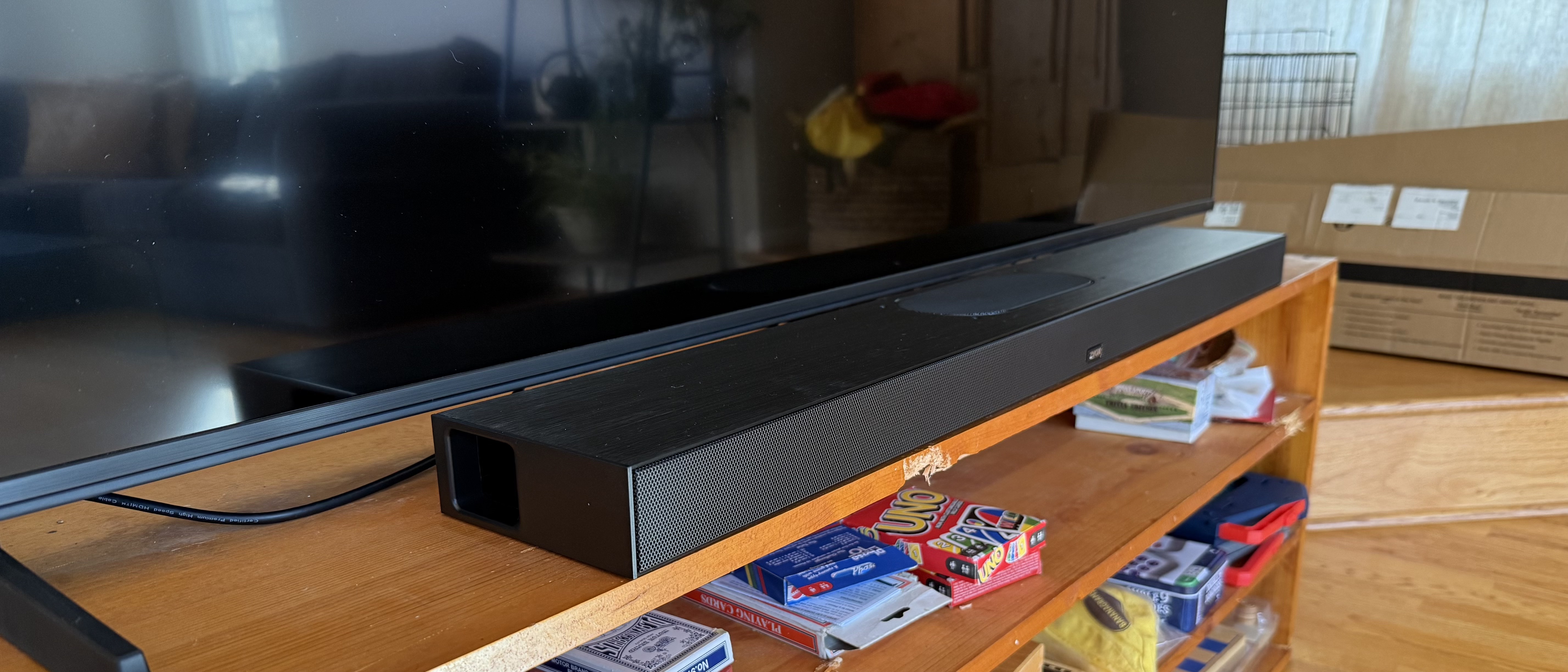 The Zvox AccuVoice AV855 soundbar pictured on a wooden cabinet under a TV