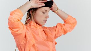 A woman wearing a black cycling cap and peach coloured waterproof rain jacket