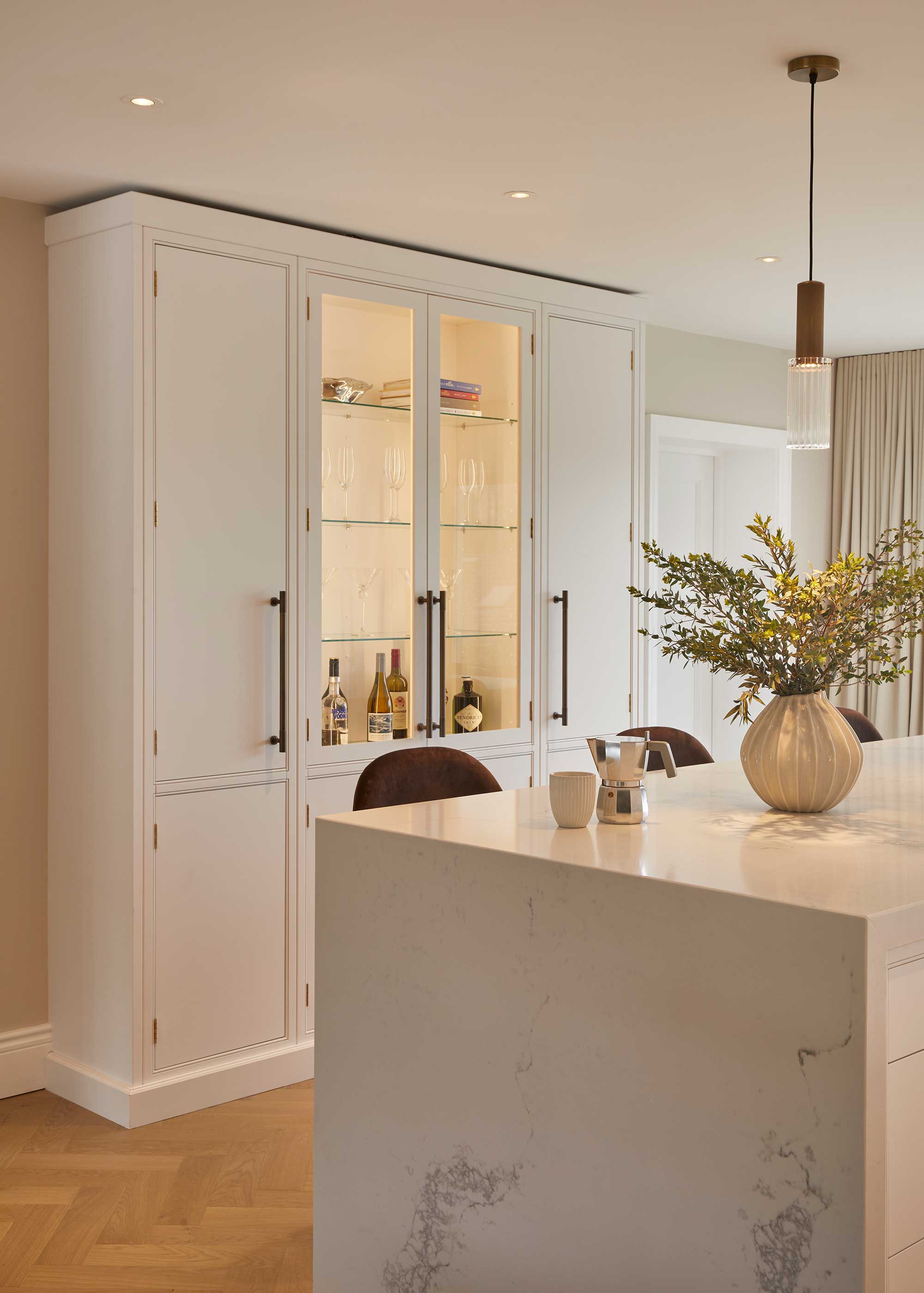 white kitchen with marble waterfall island and glass cabinet with lighting