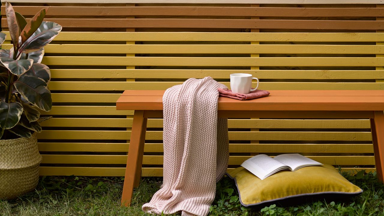 A painted wooden outdoor bench in front of painted garden fencing