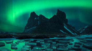 The aurora glows green over an ice-studded lake in the winning photograph in the Aurorae category.