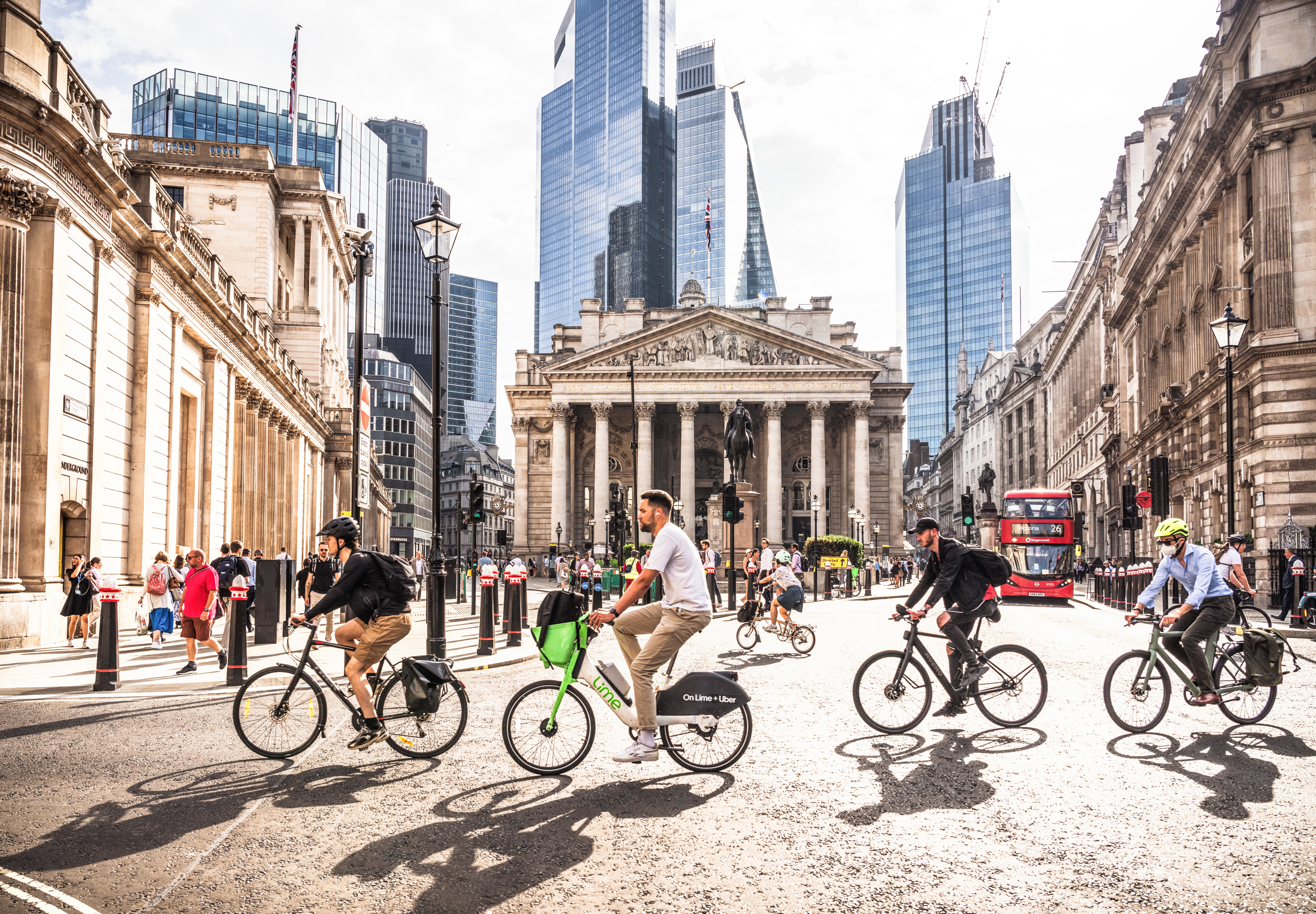 Four male cyclists bike through the City of London, in front of the Bank of England building