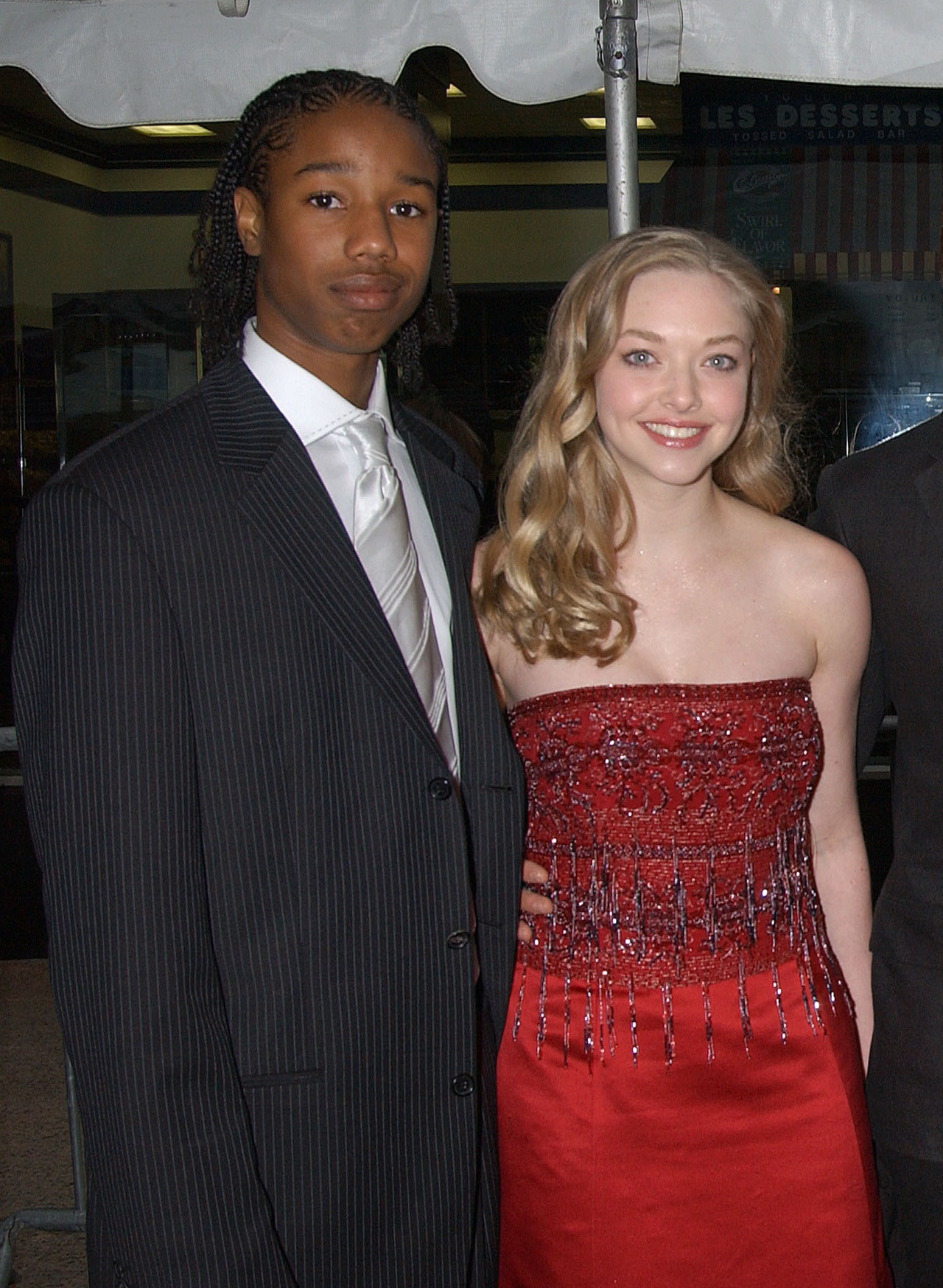 Young Michael B Jordan and Amanda Seyfried attending an All My Children event in 2004. He's in a pinstriped suit with a silver tie and she has a red satin dress with a beaded overlay on.