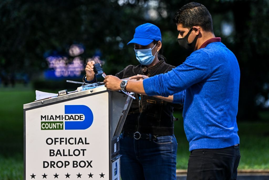 A poll worker helps a voter put as she drops off her mail-in ballot at an official Miami-Dade County drive-thru ballot drop box at the Miami-Dade County Election Department in Miami, Florida