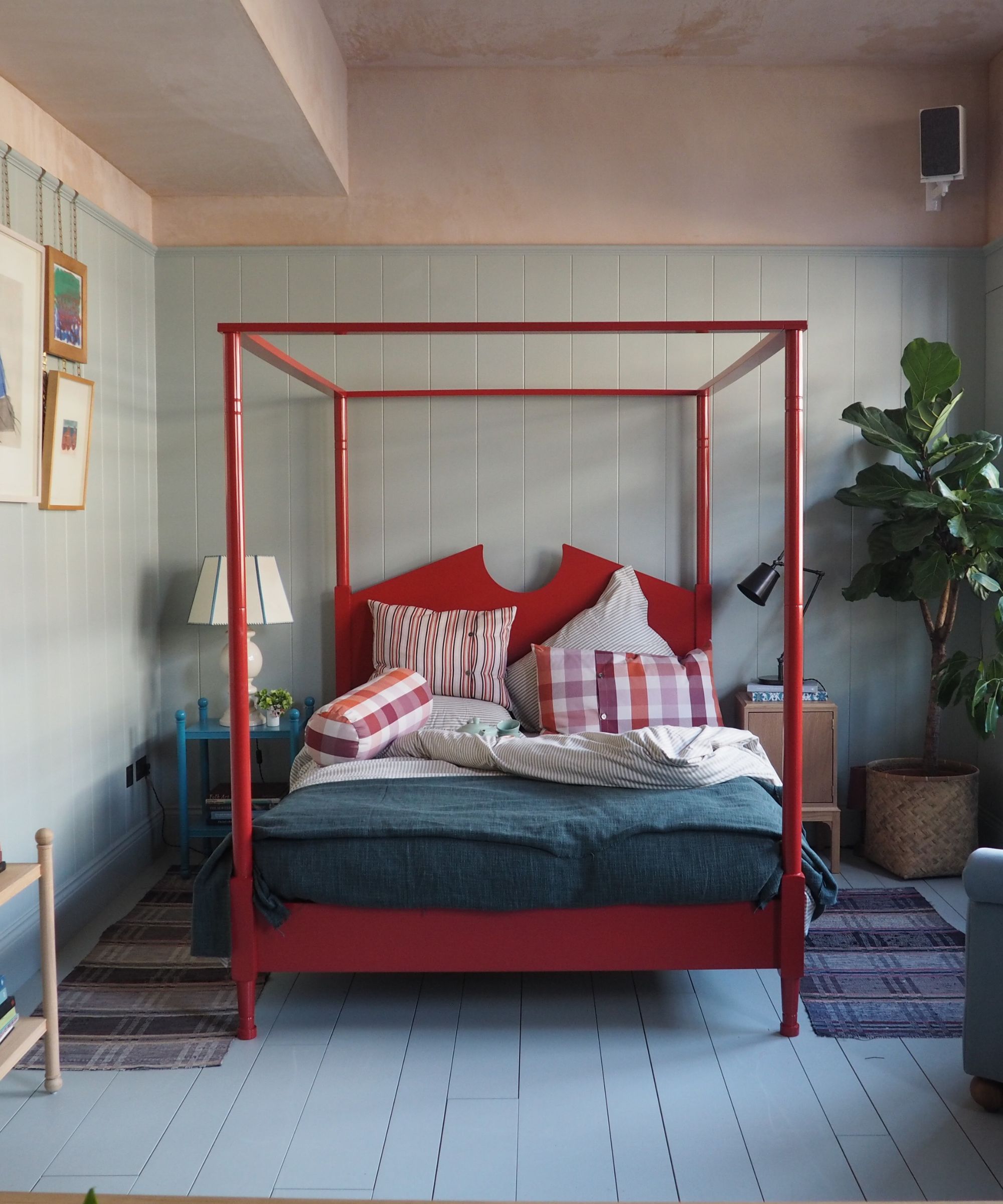 A red four poster bed in a room with blue painted floorboards